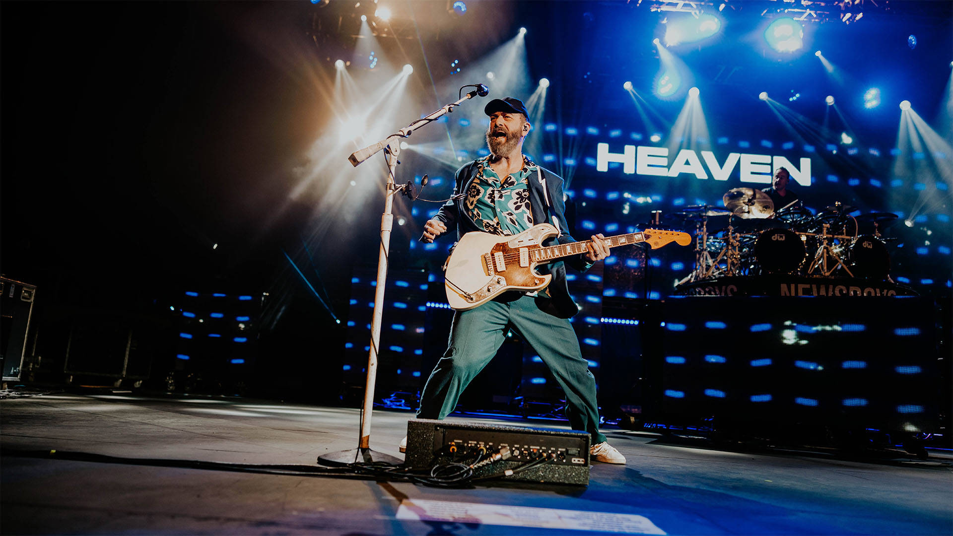 A man with light complexion, a beard and a black hat playing guitar.