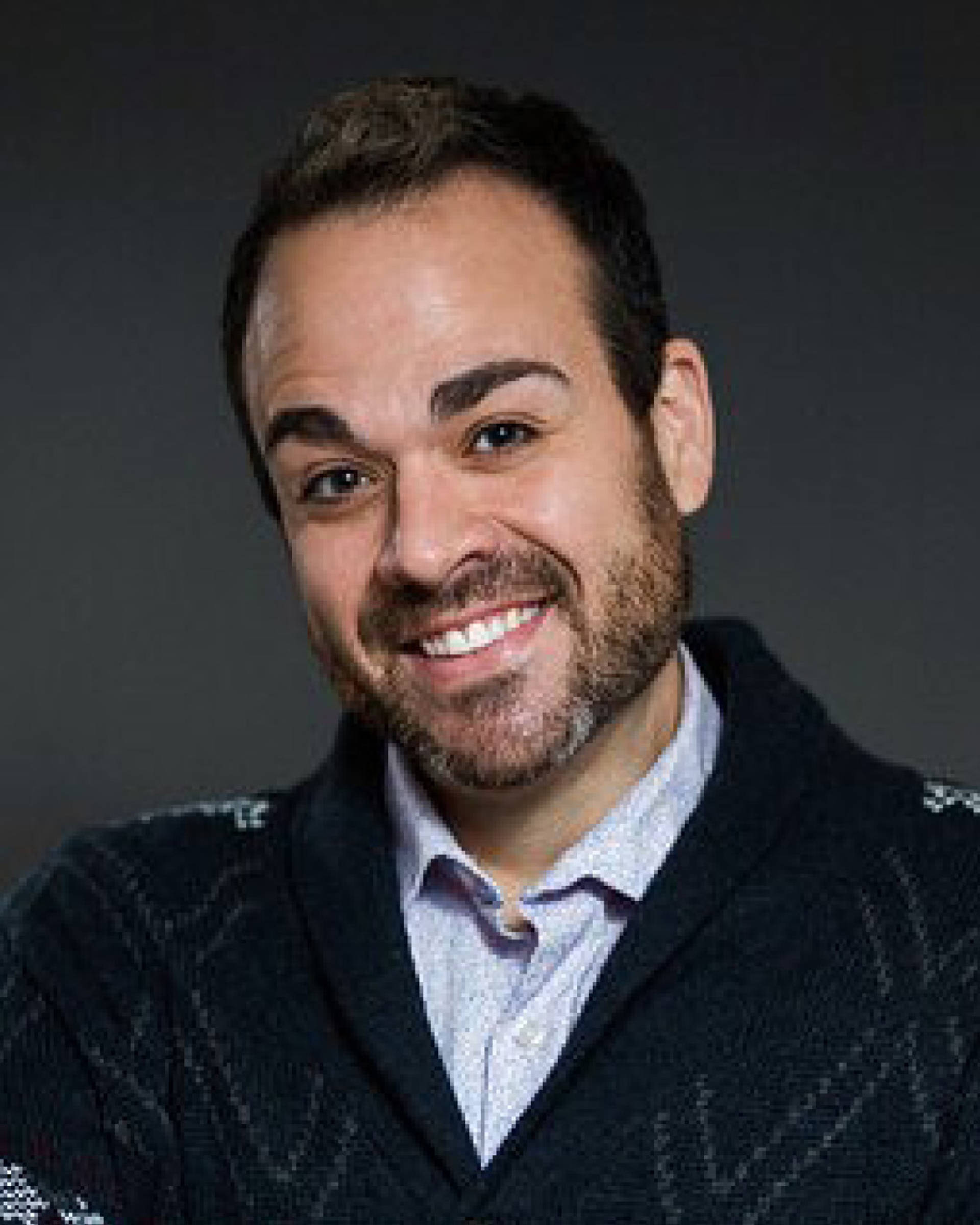 Headshot of a caucasian man with short dark hair, dark eyes, a beard, and a sweater dress shirt combo.