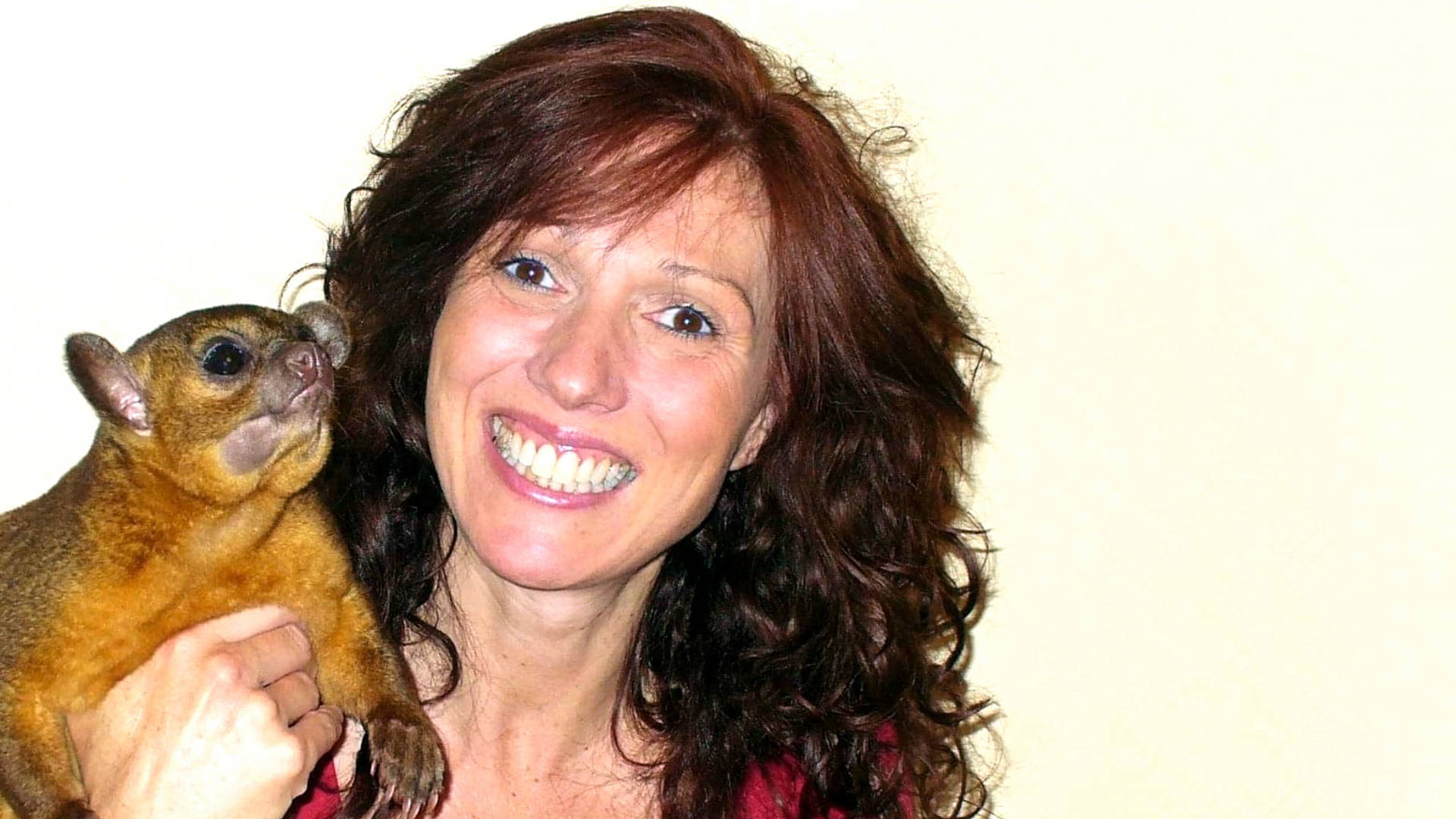 A caucasian woman with reddish brown long hair holding a small furry animal.