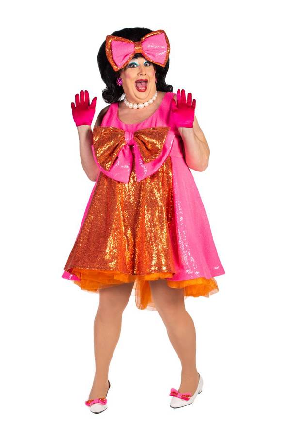 A drag performer with big dark hair, a large bowtie on their head, and a pink outfit striking a surprised pose.