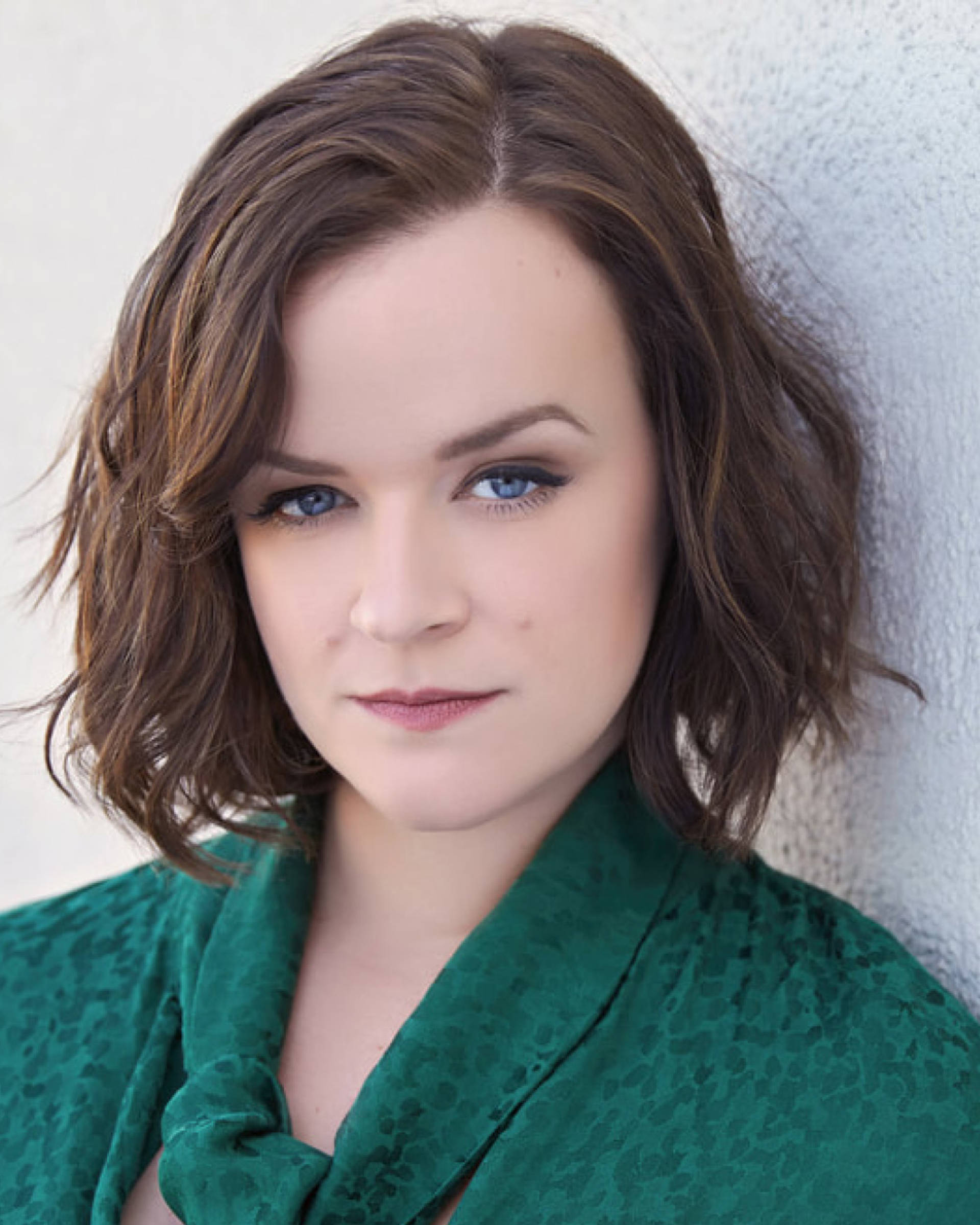 Headshot of a caucasian woman with medium brown hair, blue eyes, and a green top.