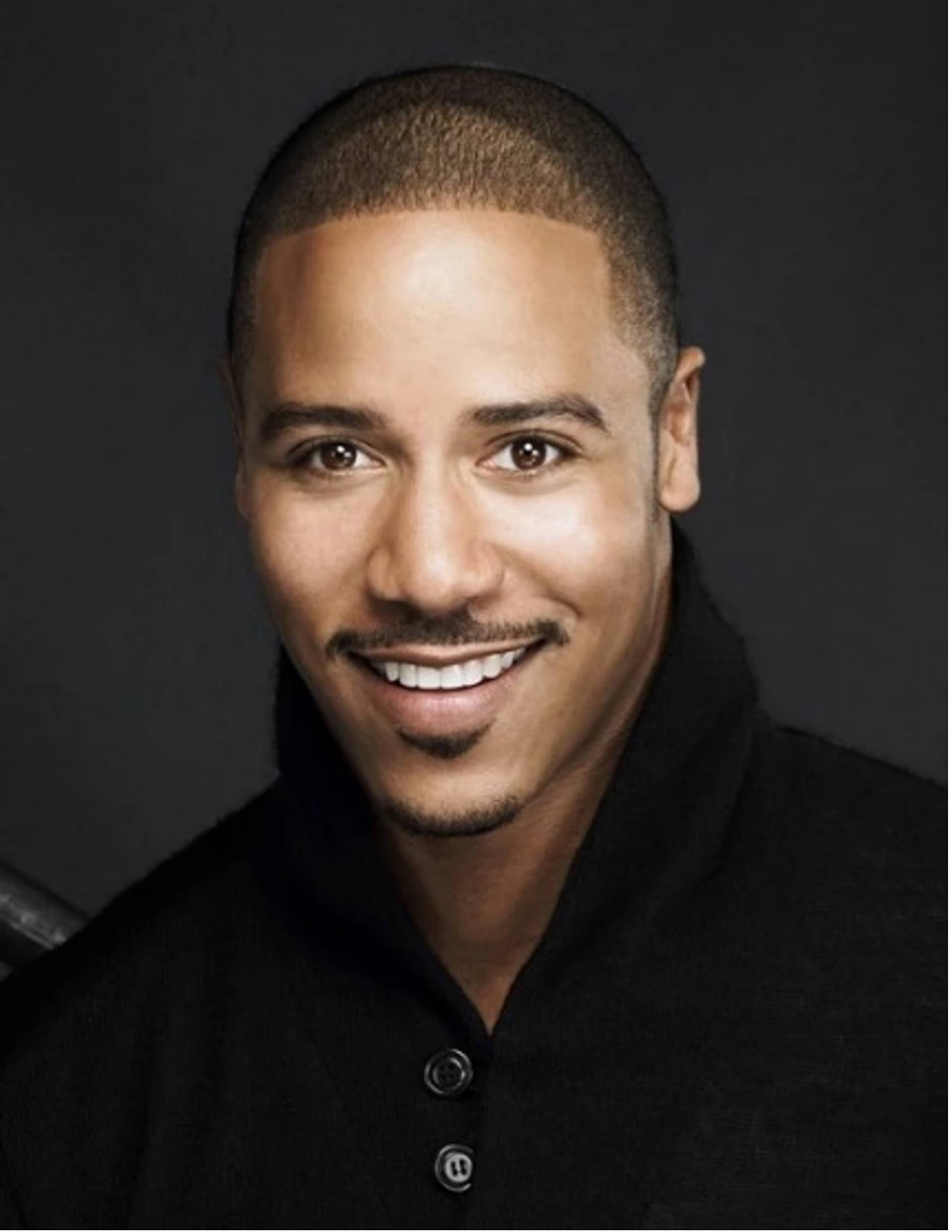 Headshot of young smiling african american man with short dark hair, brown eyes, and a moustache. in a dark top.