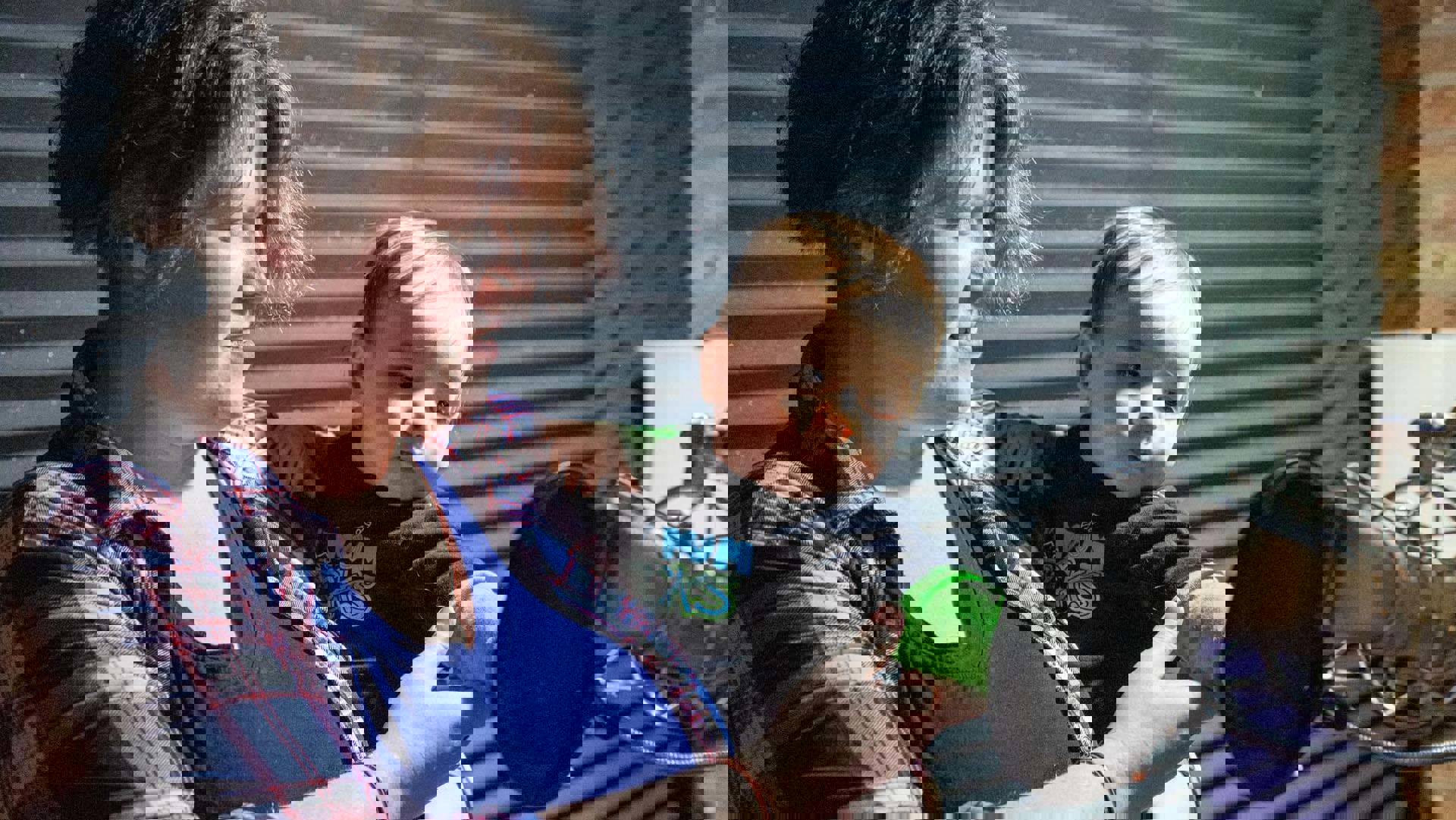 A woman with light complexion and medium length brown hair in a plaid shirt holding a baby touching a microphone