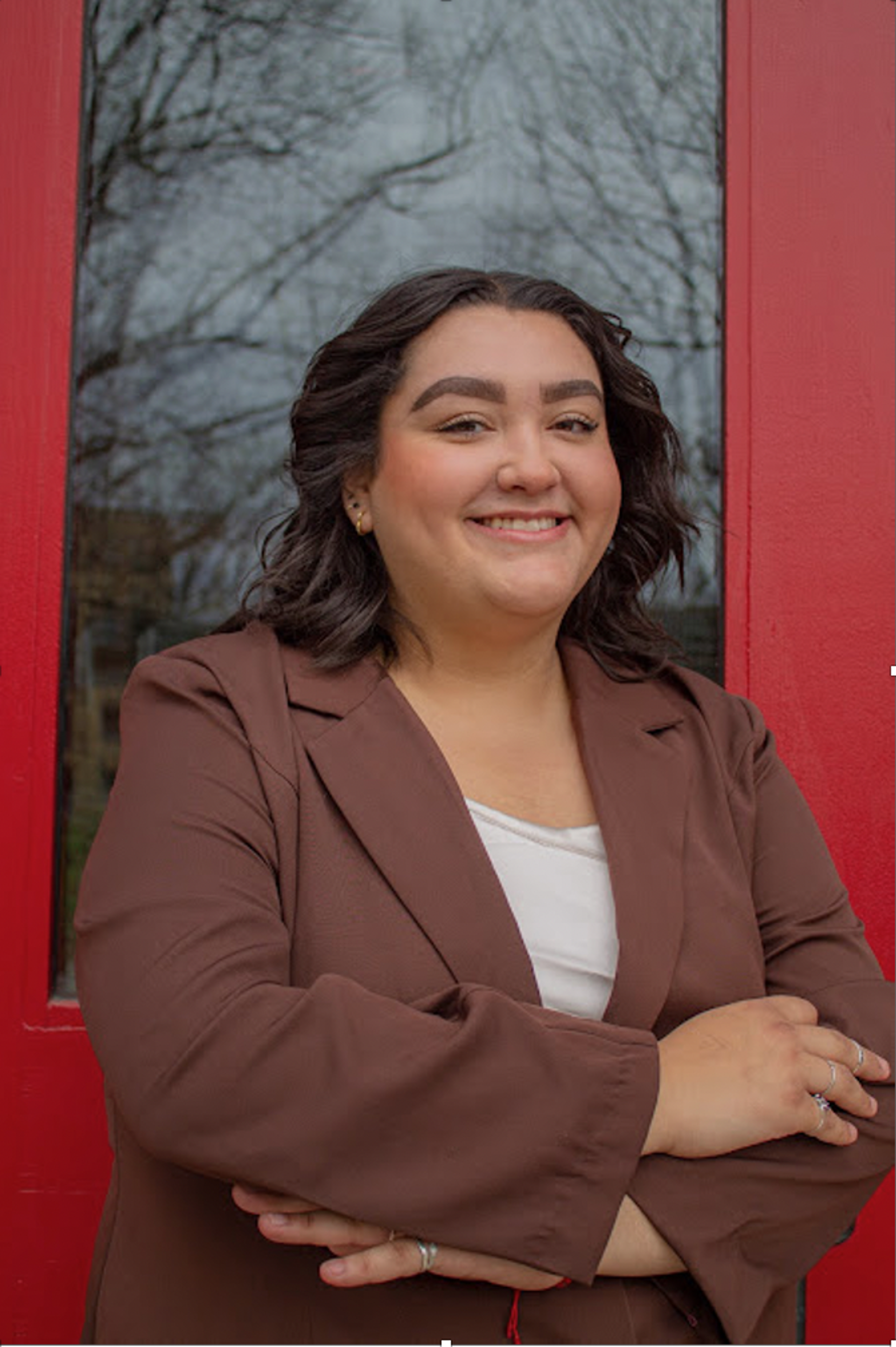 Headshot of a young woman with medium toned skin, long dark hair, and brown eyes. She is wearing a tan blazer and cream top.