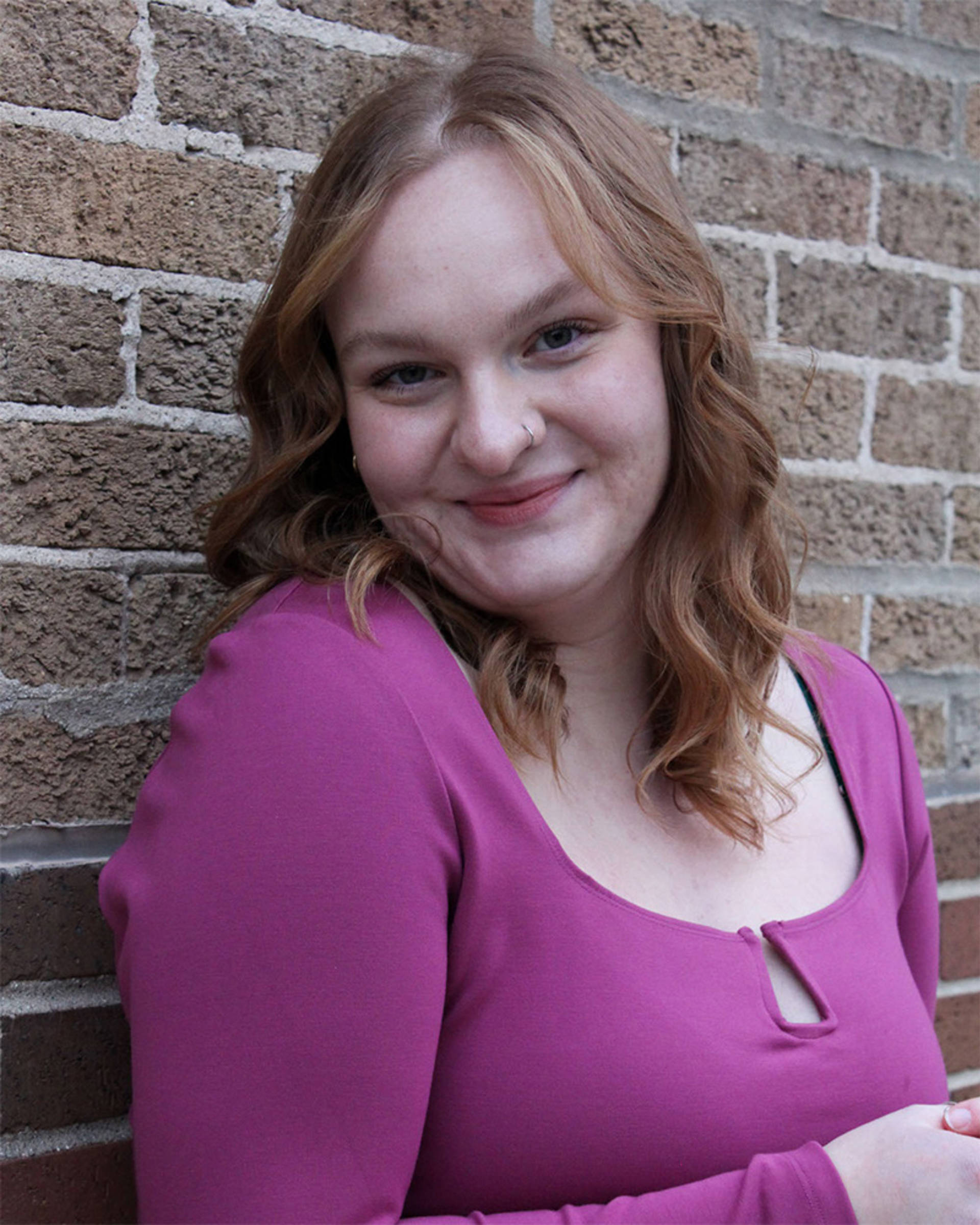 Headshot of a woman with light complexion, red hair, dark eyes and a pink top.