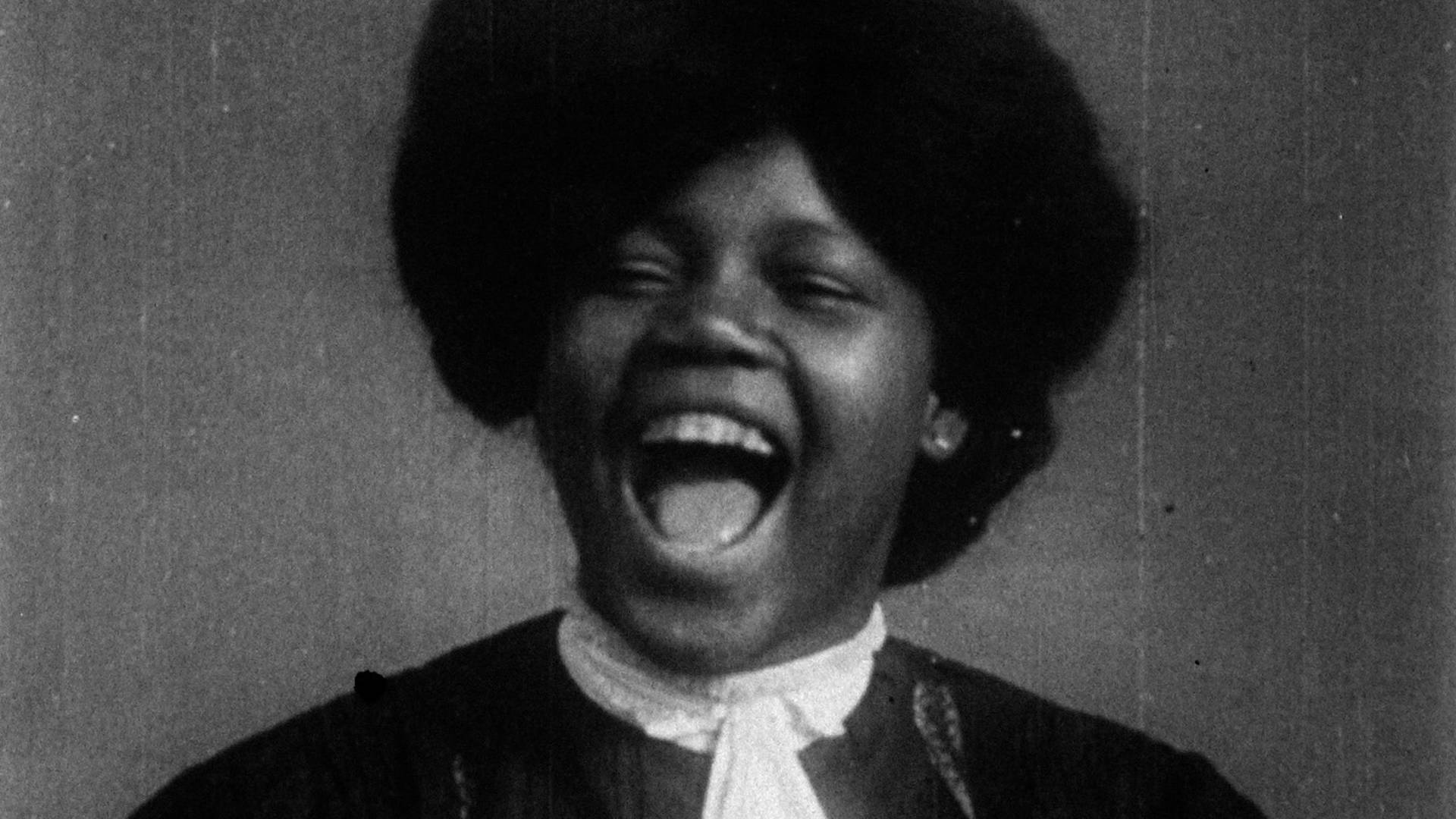 vintage black and white headshot of a dark complexion woman with medium dark hair. Her mouth is wide open and her face shows delight.