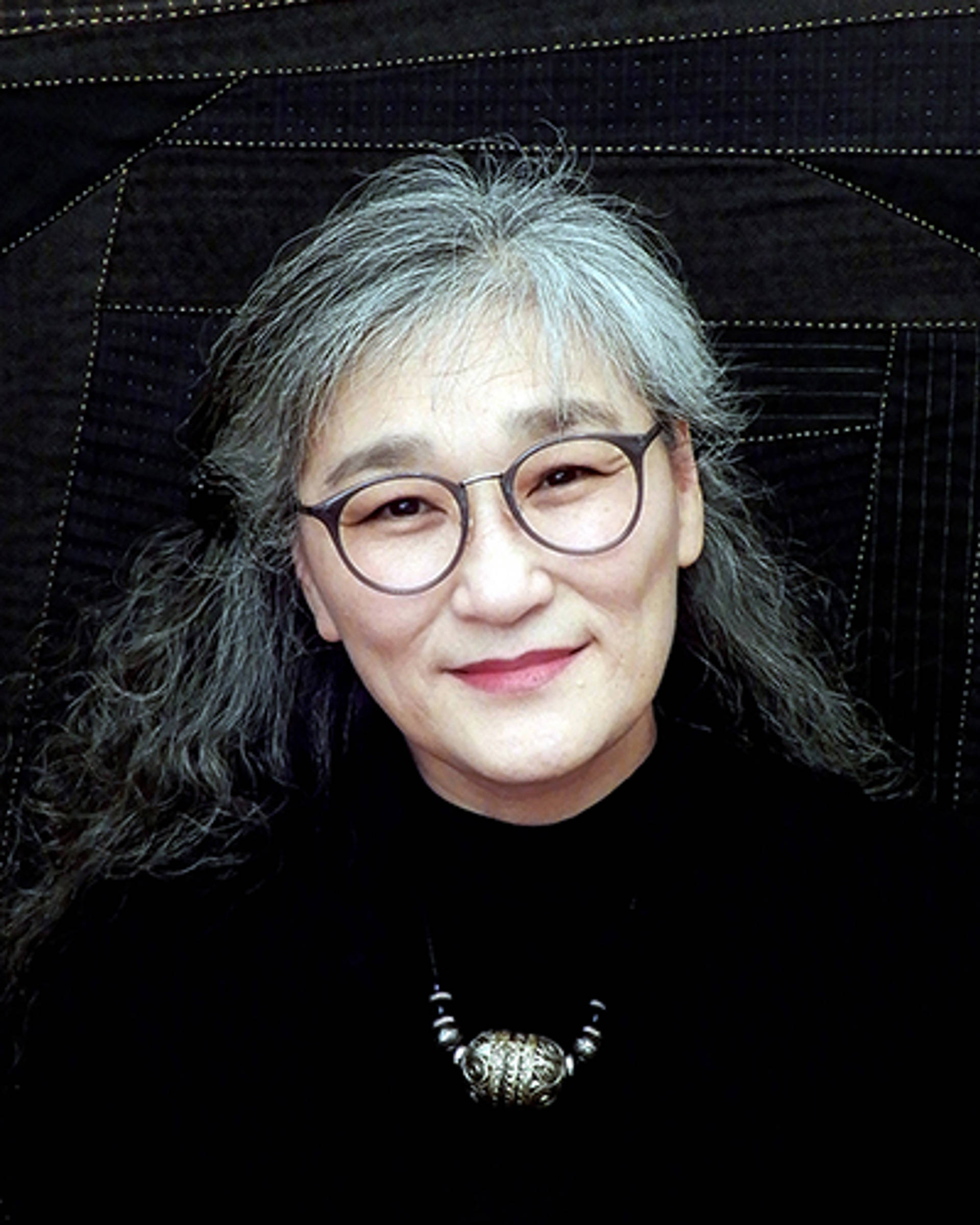Headshot of an Asian American woman with black and grey hair, dark eyes and glasses on. She is wearing a black top.