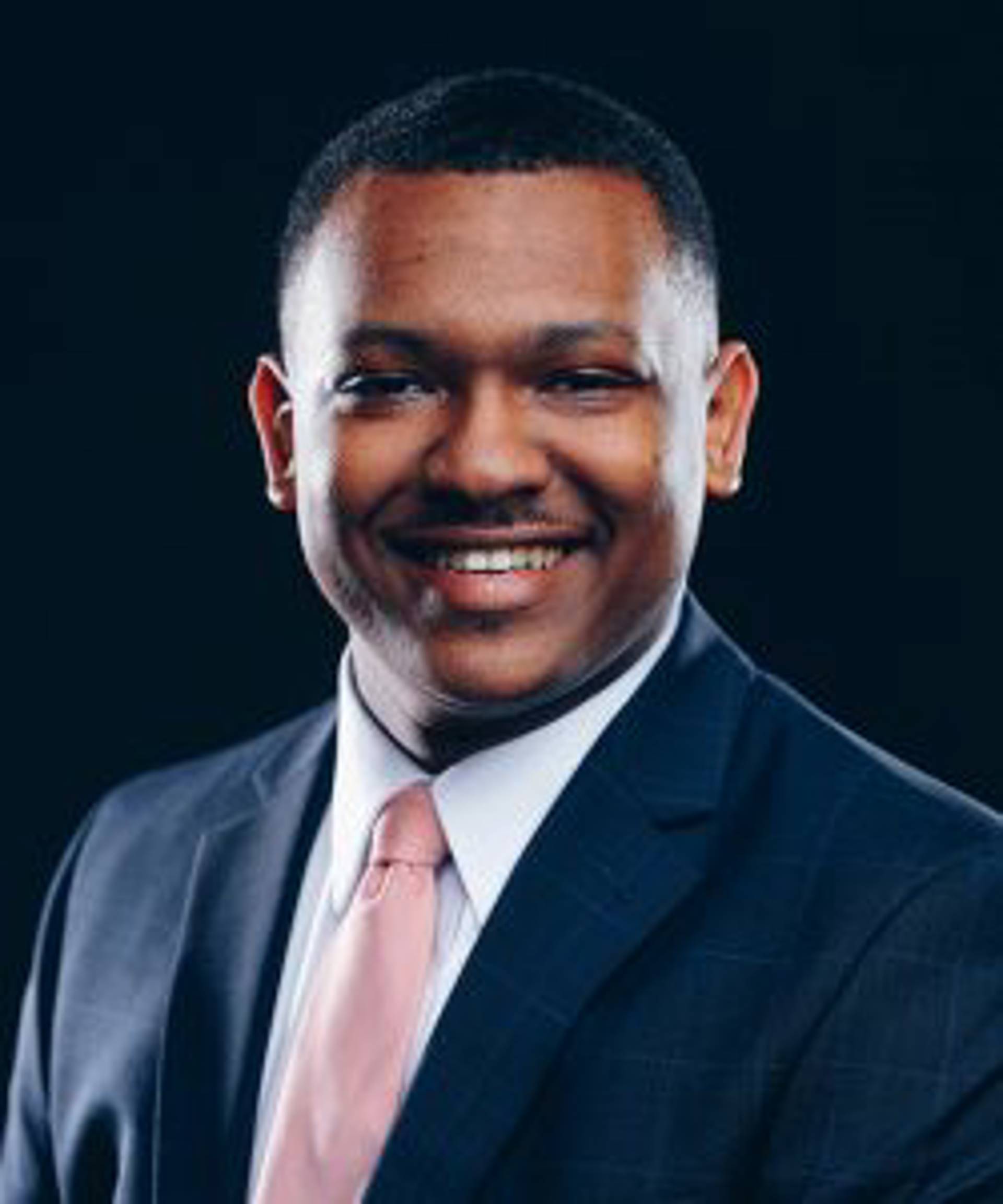 Headshot of an African American man with dark eyes and a short hair in a dark blue suit