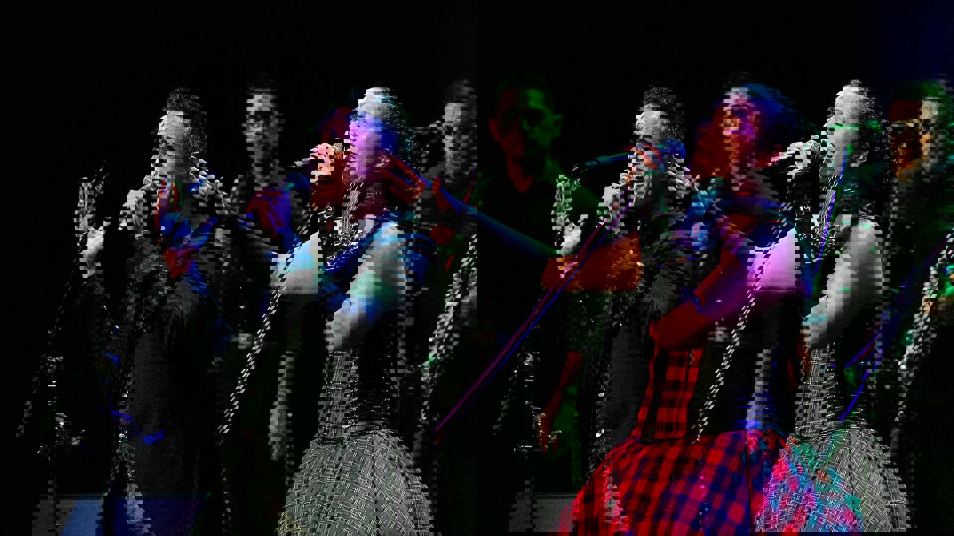 A man and woman with medium complexion and black and white face paint sing passionately into microphones and gesture toward the stage.