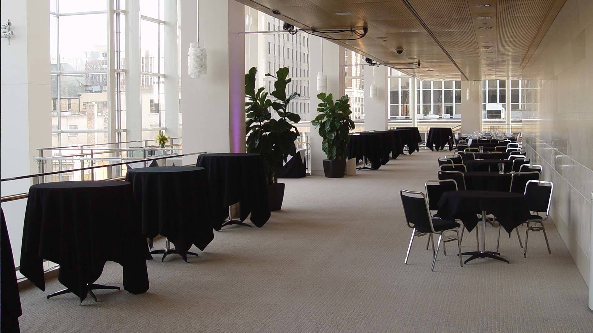 Tables with black tablecloths in a large white hall way. Green plants decorate the space.
