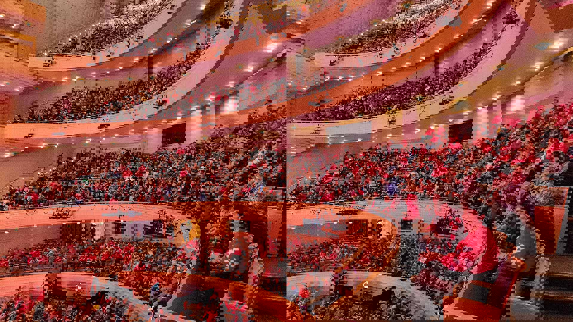 Filled upper levels of Overture Hall's seating, students and teachers wearing red for the UW marching band performance.