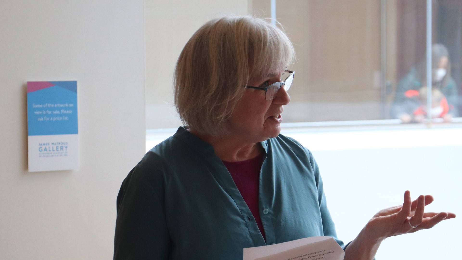 A middle aged white woman with short grey hair and glasses in a blue blouse.