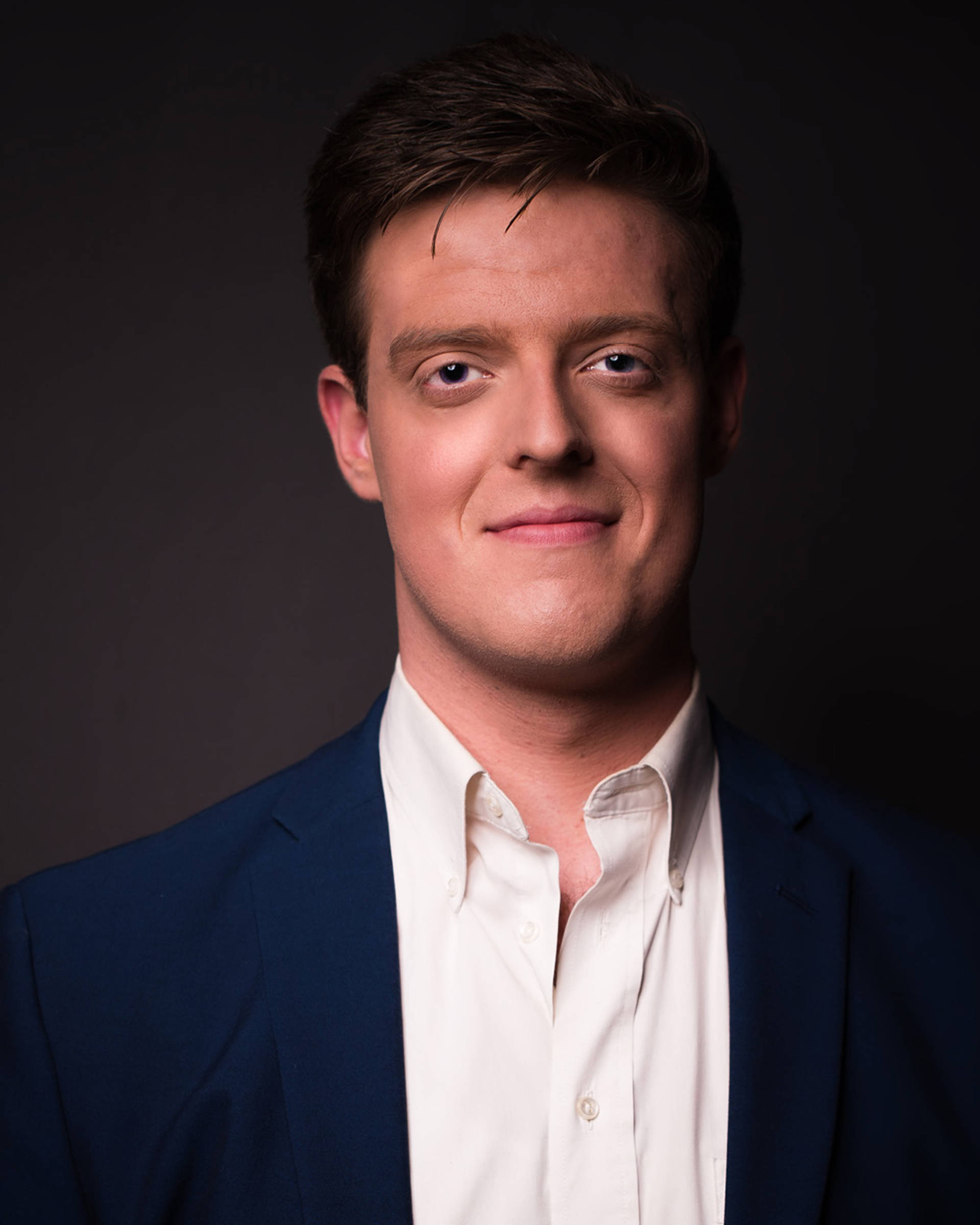 Headshot of a caucasian man with short brown hair, dark eyes and a white colored shirt and suit jacket on.