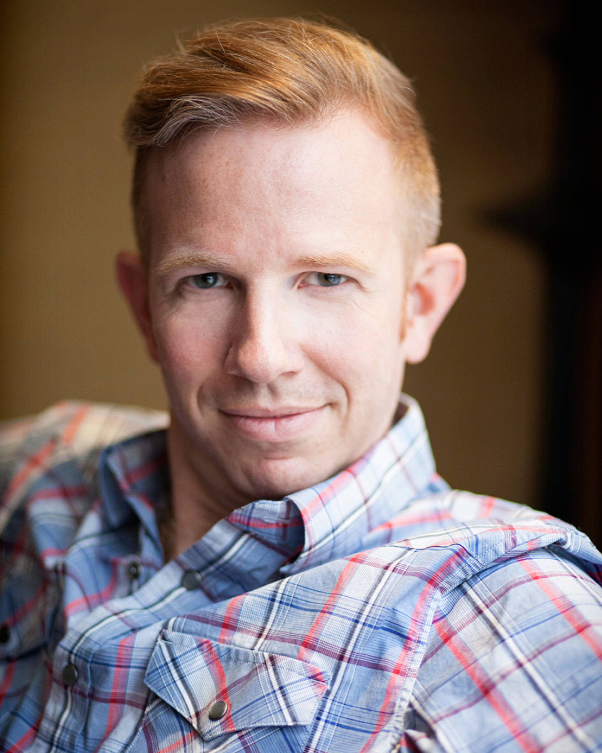 Headshot of a caucasian man with red hari, blue eyes and a plaid shirt.