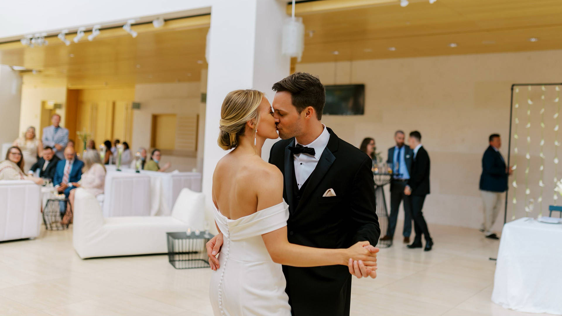 A white couple on their wedding day dance and kiss each other.