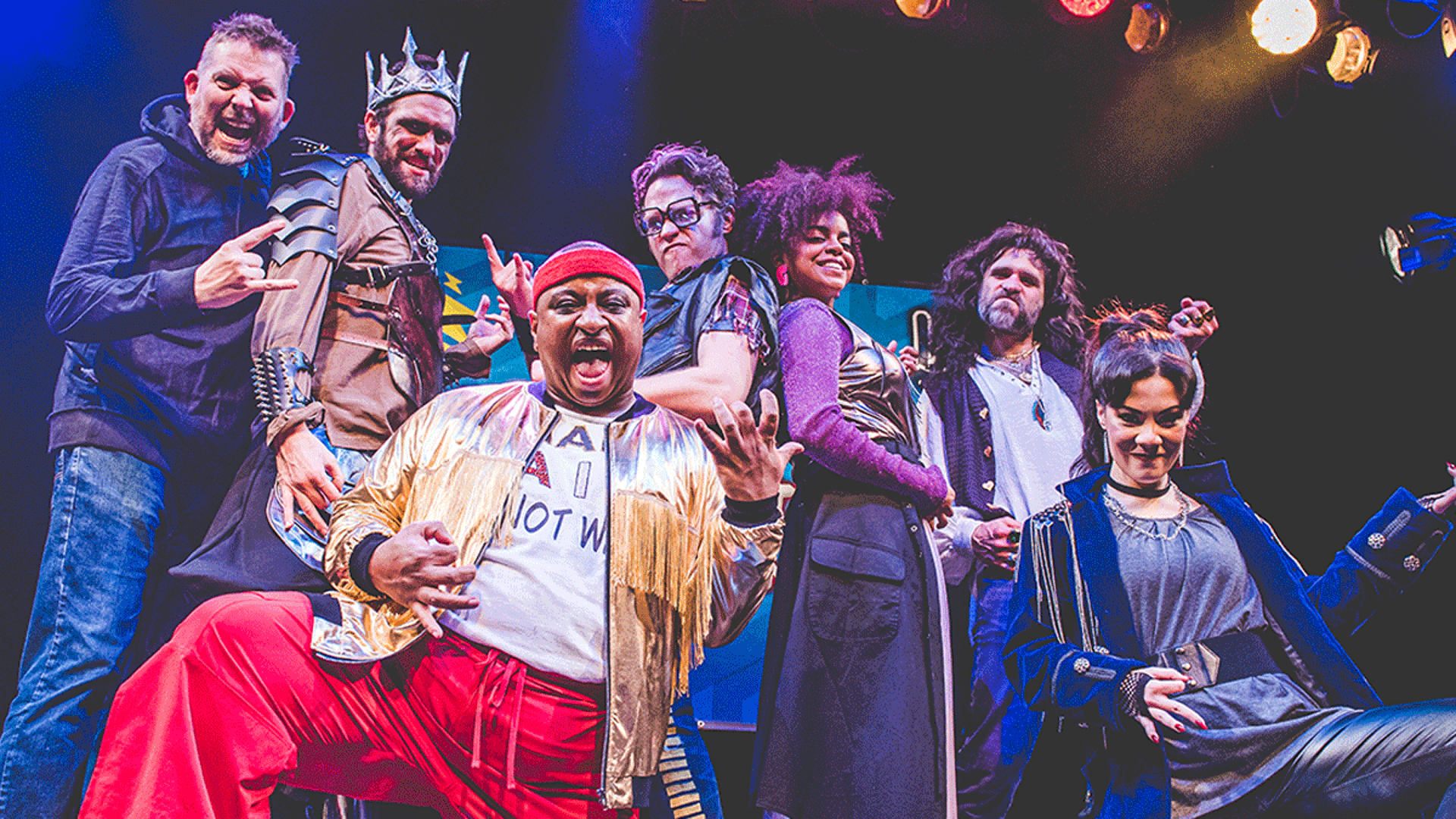 An ensemble cast photo from Forward Theater's Airness production. A group of diverse adults in flamboyant rock costumers "air guitaring"