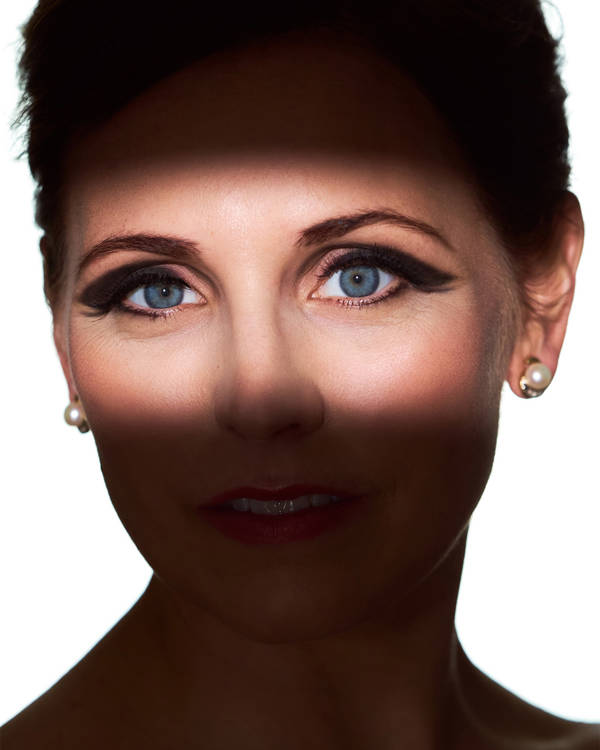 Headshot of a caucasian woman with blue eyes. There is a shadow across her face, except for her eyes, which are illuminated