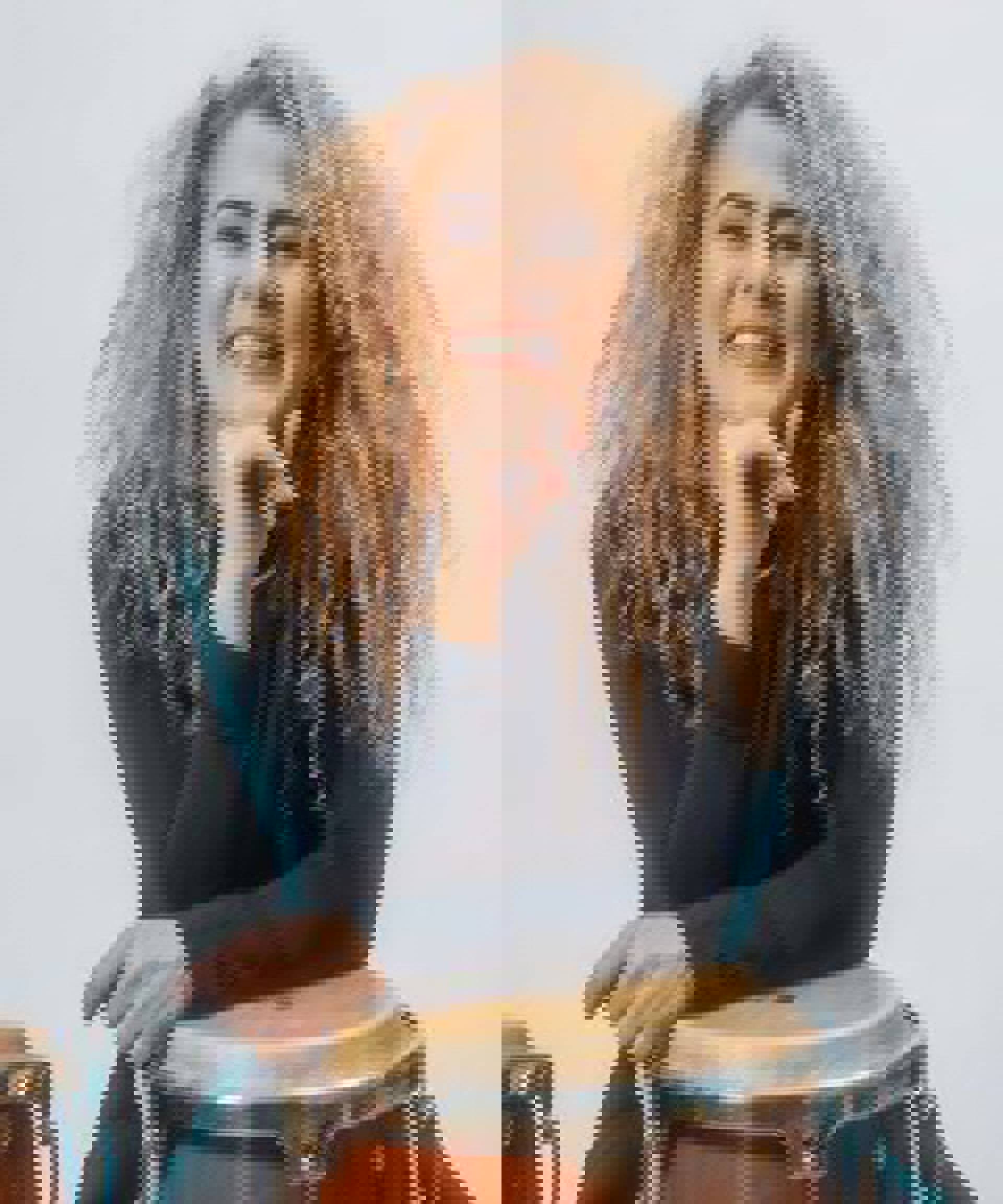 A woman with curly blond hair smiles and is sitting behind a conga.