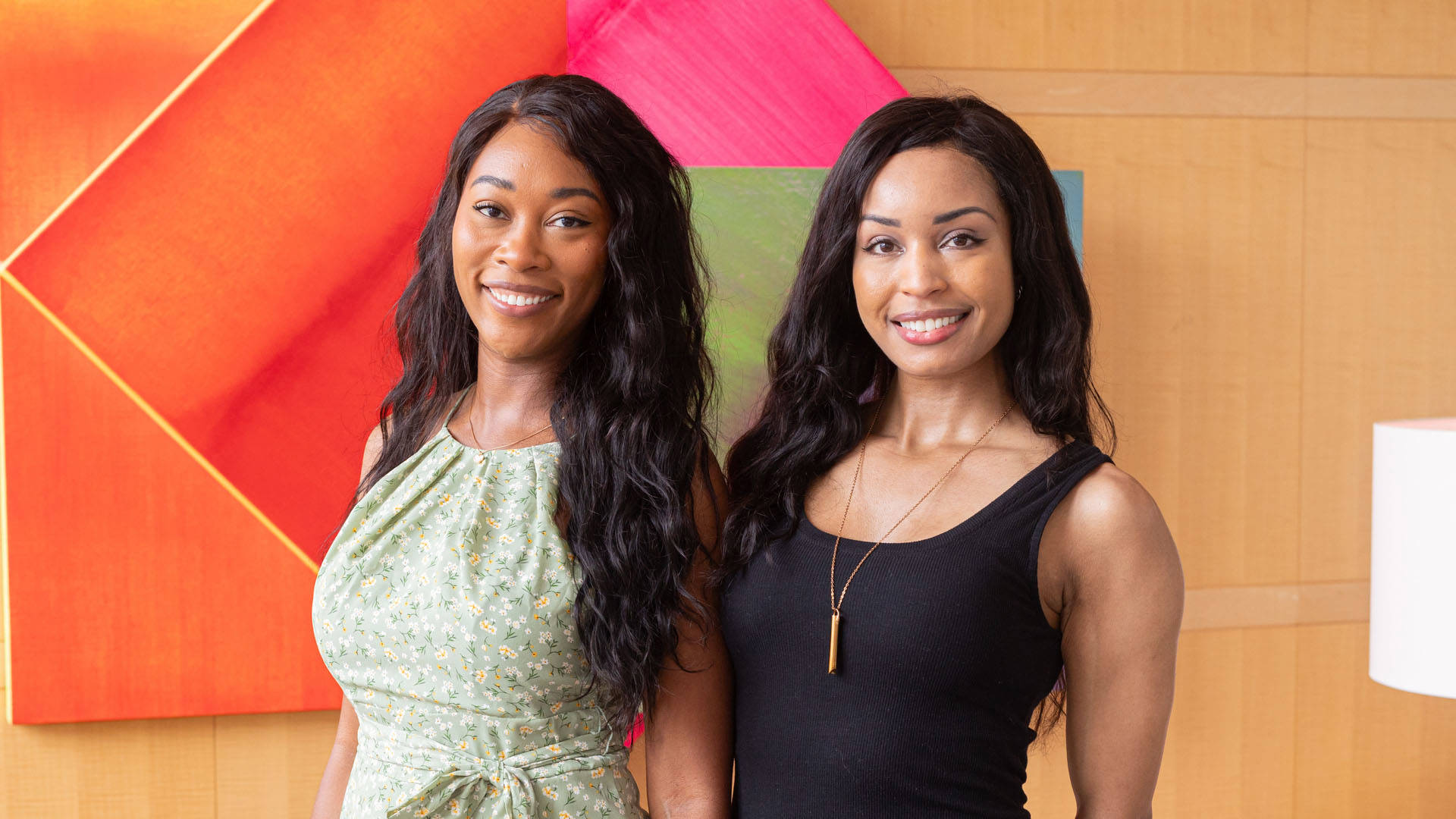 Two young african american women stand together smiling for a photo.