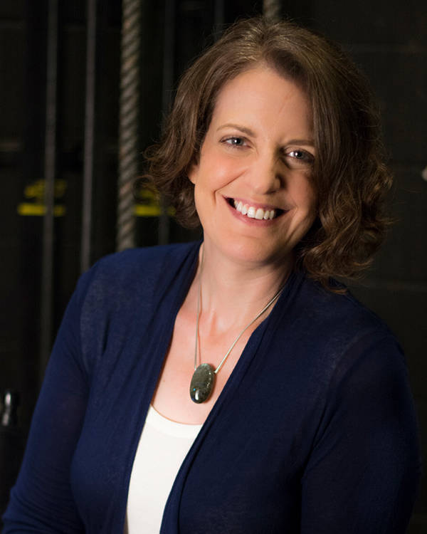 Headshot of a smiling caucasian woman with brown eyes and brown hair. She is wearing a blue cardigan and white top.
