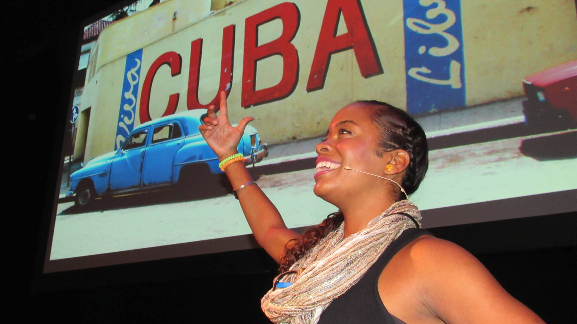 A hispanic woman smiling as she stands in front of a screen that says "CUBA"