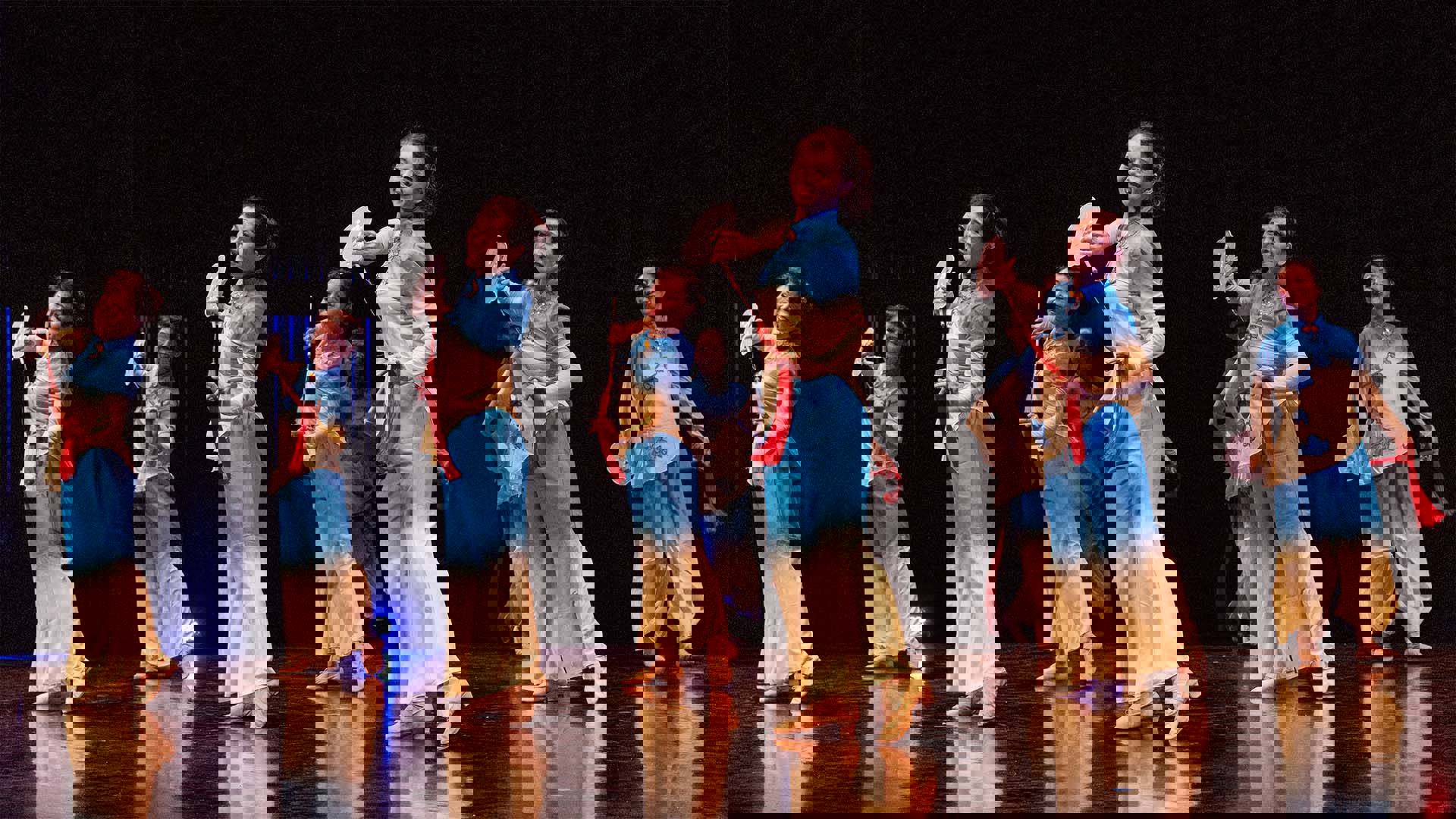 Seven women in matching blue and beige outfits dancing on a dark stage.