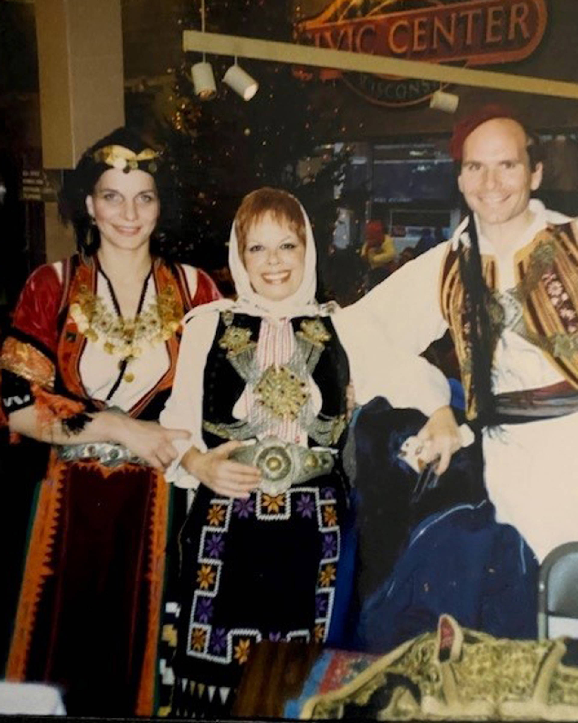 Three people in multicolor traditional Greek dance outfits posing for a photo.