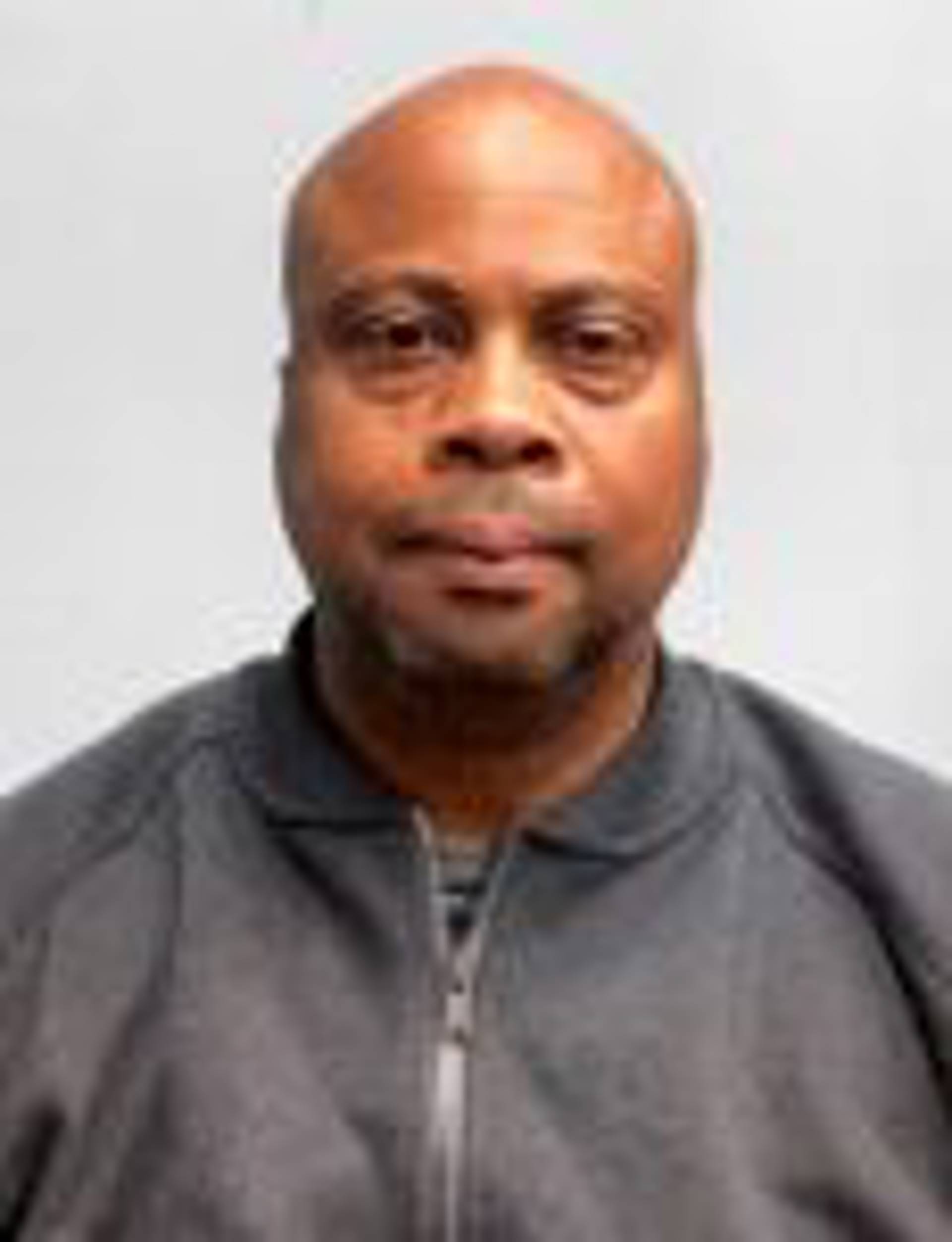 Headshot of a middleaged african american man with a bald head and a grey jacket.