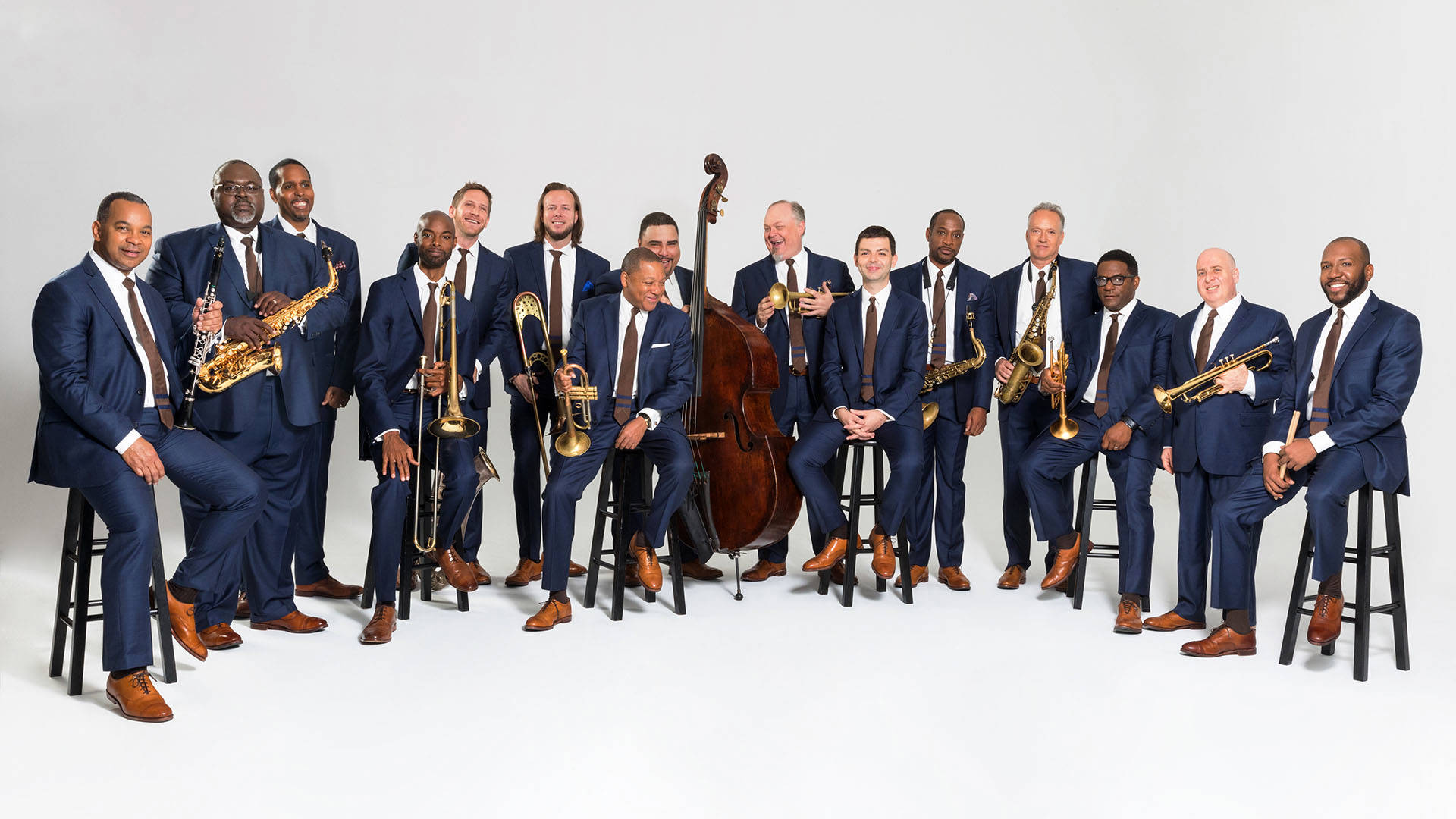 A smiling group of men in matching blue suits holding their various jazz instruments against a white background.