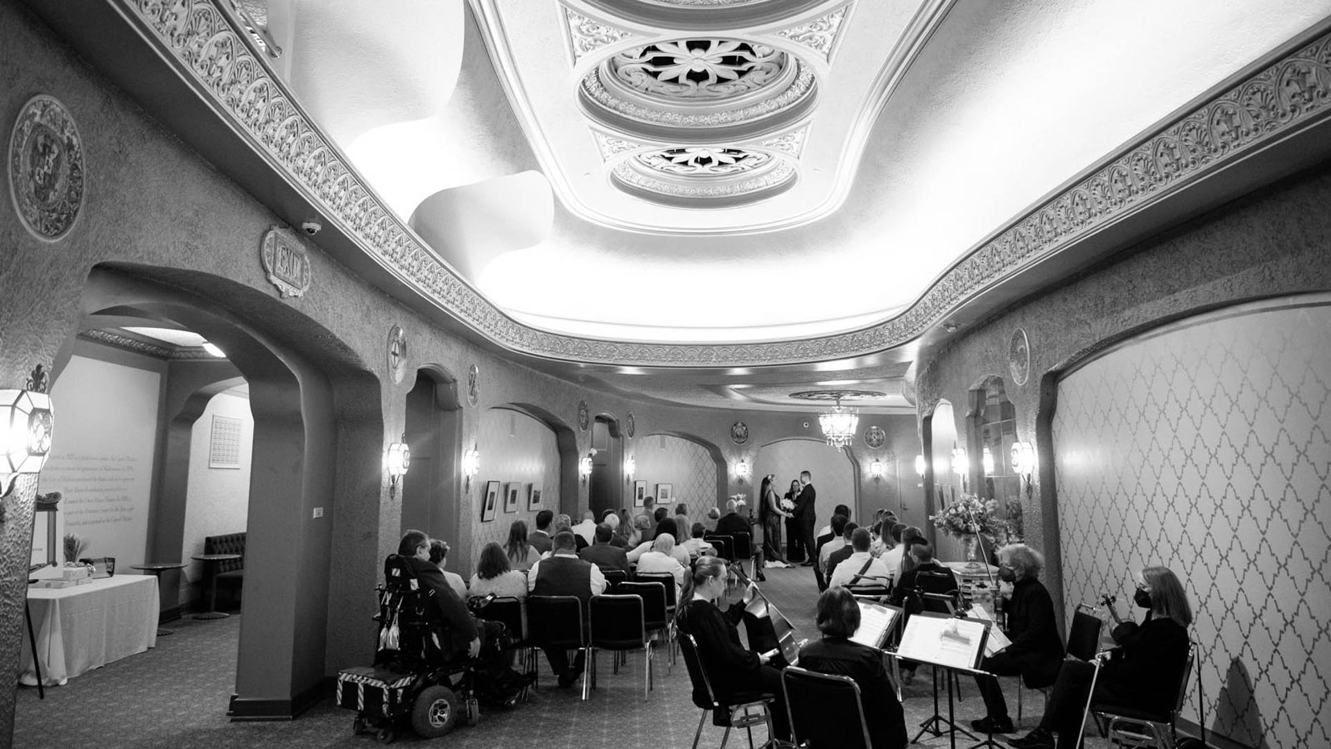 Grayscale photo of a wedding ceremony in Capitol Theater lobby. There is a string quartet.