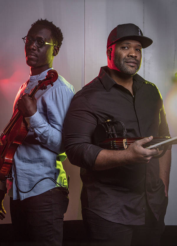 The two members of Black Violin. They are both holding a violin and a bow. 