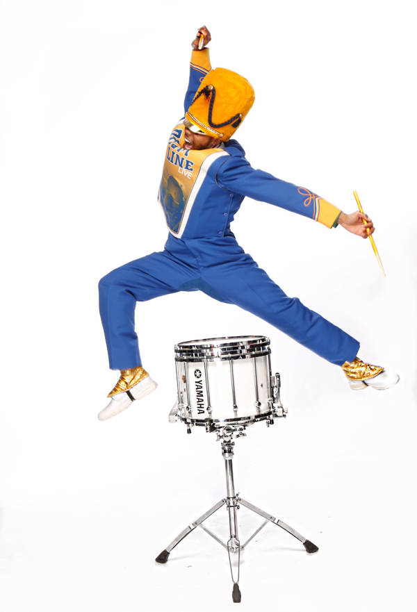 A Black drummer mid leap and mid strike above a snare drum against a white background. They are wearing a blue marching band uniform with yellow and gold accents.